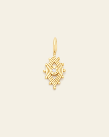 Hero image of a gold evil eye pendant with a round Cubic Zirconia stone in the middle of the eye on a cream background.