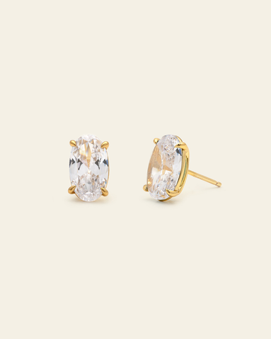 Clear oval stud earrings in a gold prong setting featuring faceted clear cubic zirconia stones with elegant sparkle on a neutral background.