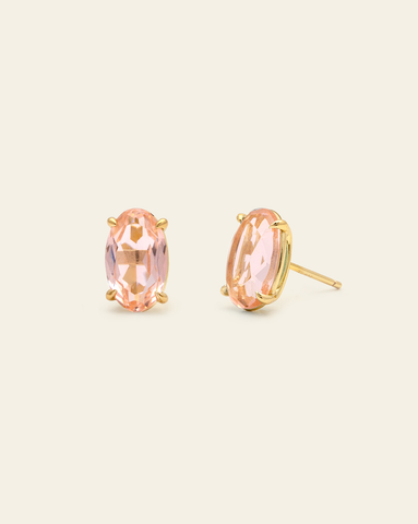 Blush pink oval stud earrings in a gold prong setting featuring faceted pink stones with elegant sparkle on a neutral background.