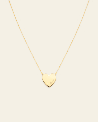 Hero Image of a gold vermeil Mama Heart Necklace with the Mama engraving on it on a cream background.