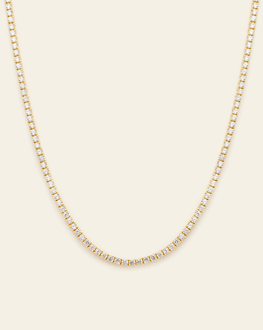 A Gold Vermeil prong set tennis necklace with CZ stones displayed on a cream background.