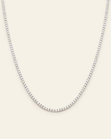 Sterling silver tennis necklace featuring prong-set sparkling cubic zirconia stones on a cream background.