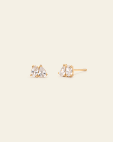 Hero Image of gold vermeil studs earrings with twin pear and marquise-cut white stones, representing love and balance in a dainty double-stone design on a cream background.