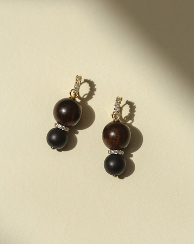 Close up picture of wood charms with a gold vermeil pave link in the middle. Attached to gold vermeil huggie with cubic zirconia on a cream background.